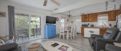 Una sala de estar amplia con ventilador de techo, un comedor con un aparador azul y una cocina con muebles de madera.