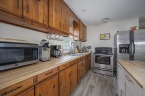 A kitchen with wooden cabinets, a stainless steel refrigerator, a microwave, a coffee maker, and a stove. - 7602- Drydock, Dog-Friendly Avon Cottage Near the Beach (Avon)