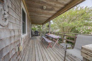 A wooden deck with a covered area, outdoor furniture, and a view of trees and flowers. - 7602- Drydock, Dog-Friendly Avon Cottage Near the Beach (Avon)