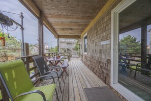 A covered outdoor area with a wooden deck, outdoor seating, and a view of a residential building. - 7602- Drydock, Dog-Friendly Avon Cottage Near the Beach (Avon)