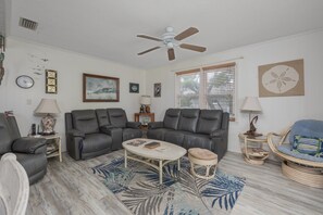 A living room with a sectional sofa, a coffee table, a side table, a floor lamp, a wall clock, framed artwork, and a ceiling fan. - 7602- Drydock, Dog-Friendly Avon Cottage Near the Beach (Avon)