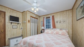 A bedroom with a bed, a ceiling fan, a television, and wooden paneling. - 7602- Drydock, Dog-Friendly Avon Cottage Near the Beach (Avon)
