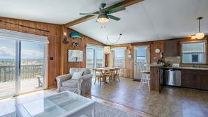 A spacious living area with a glass coffee table, a sofa, a dining table with chairs, and a kitchen area with wooden cabinets and a dishwasher. - 7913-Southern Comfort - Hatteras Oceanfront Escape | Dog Friendly (Hatteras)
