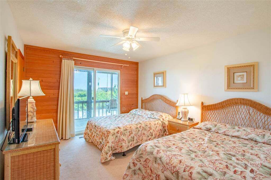 Une chambre avec deux lits, un ventilateur de plafond et une grande fenêtre avec des rideaux.