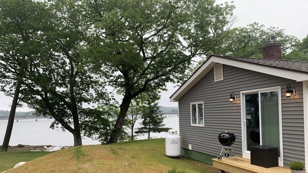A small house with a deck, a grill, and a water heater. - Cottage in Edgecomb - Waterfront Holiday Getaway (Edgecomb)