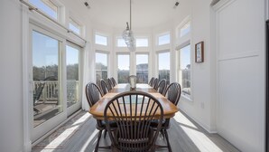 Een eetkamer met een grote houten tafel, meerdere stoelen en een hangende lamp.