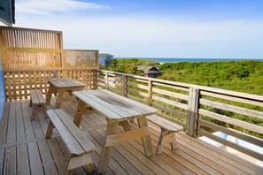 Une terrasse en bois avec des tables de pique-nique et une clôture en bois donnant sur une plage.