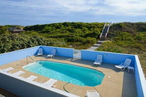 Une piscine rectangulaire bordée de bleu, entourée de chaises longues blanches.