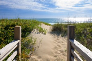 Ein Sandweg am Strand mit hölzernen Geländern, der zum Meer führt.