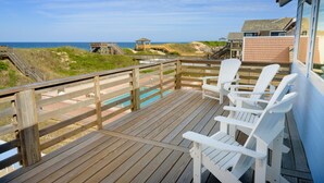 Terraza de madera con sillas blancas que da a una playa y una piscina.
