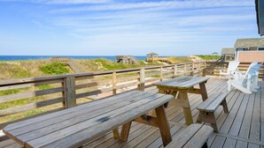 Una terraza de madera con mesas y sillas de picnic con vista a la playa.