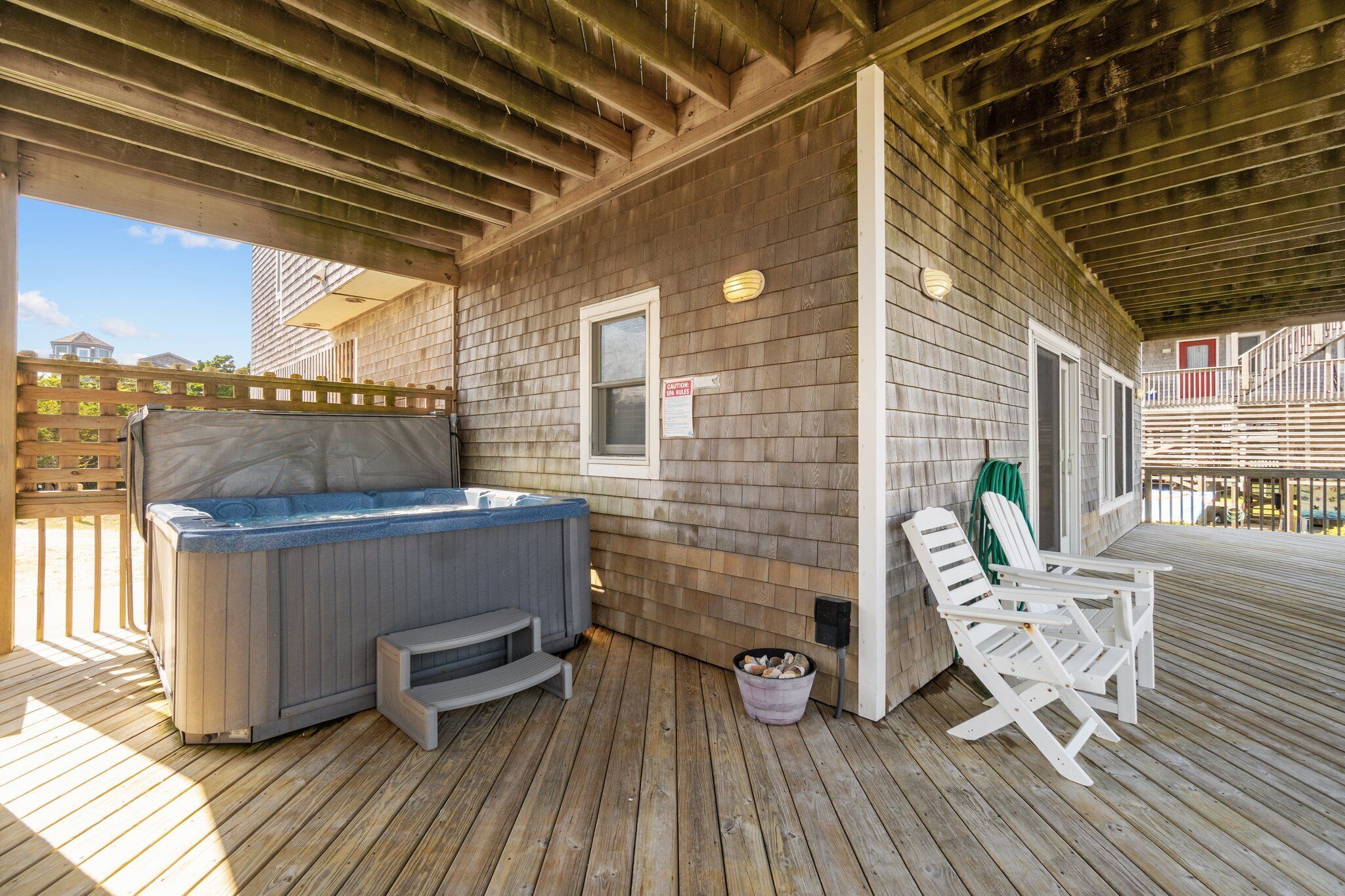 Eine überdachte Terrasse im Freien mit Whirlpool, Adirondack-Stühlen und einer Holzterrasse.