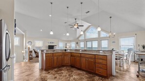 A spacious kitchen with a large island, wooden cabinets, and a ceiling fan. - 7700-Lee's Landing - Oceanfront Avon | Pool & Hot Tub | Sleeps 10 (Avon)