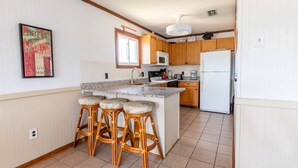 Une cuisine dotée d’un îlot central, de meubles en bois, d’un four à micro-ondes, d’un réfrigérateur et d’une fenêtre.