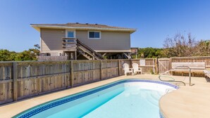 Une piscine avec une terrasse en bois, une maison dotée d’un balcon et une clôture en bois.