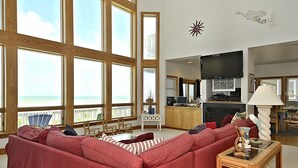 Ett rymligt vardagsrum med ett stort fönster med utsikt över havet, en bekväm röd soffa och en köksdel med en platt-TV.