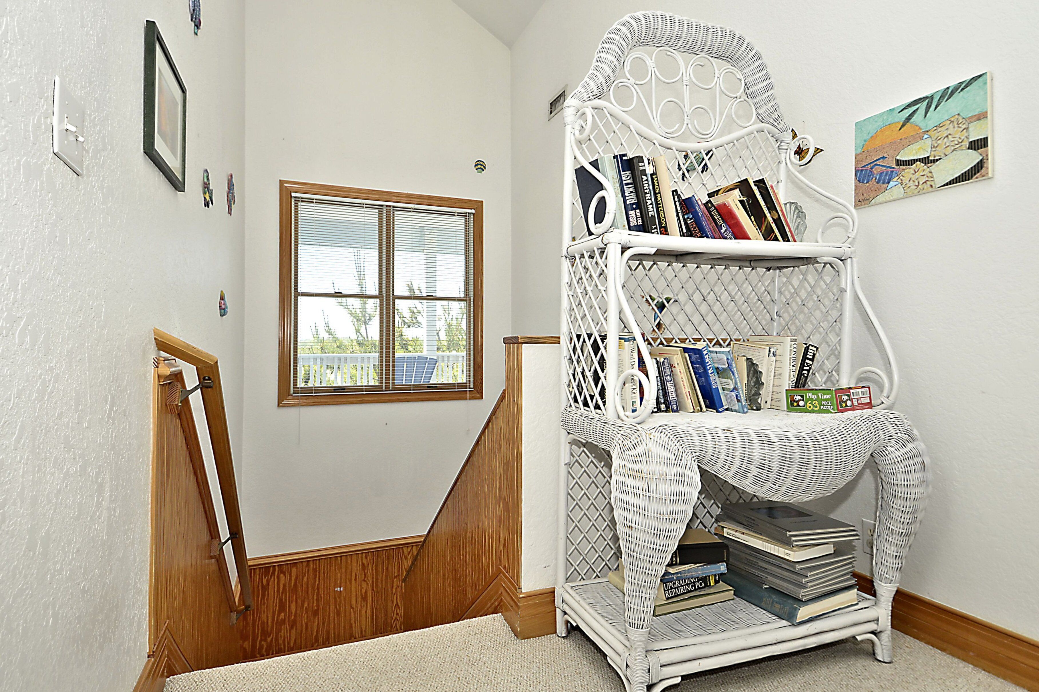 A staircase with a white wicker bookshelf filled with books and a puzzle box.