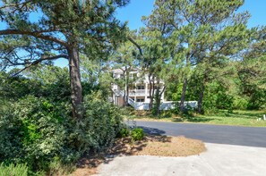 Stunning two-story house with a spacious balcony and traditional facade, set amidst mature pine trees and lush greenery.