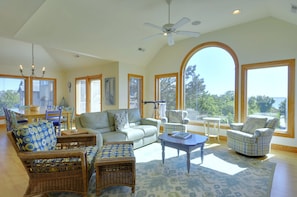 Relax in this spacious living room with a high ceiling and ceiling fan, featuring a large arched window offering a view of the outdoors.