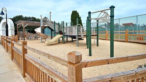 Ein Spielplatz mit Rutsche, Klettergerüsten und einem umzäunten Bereich.
