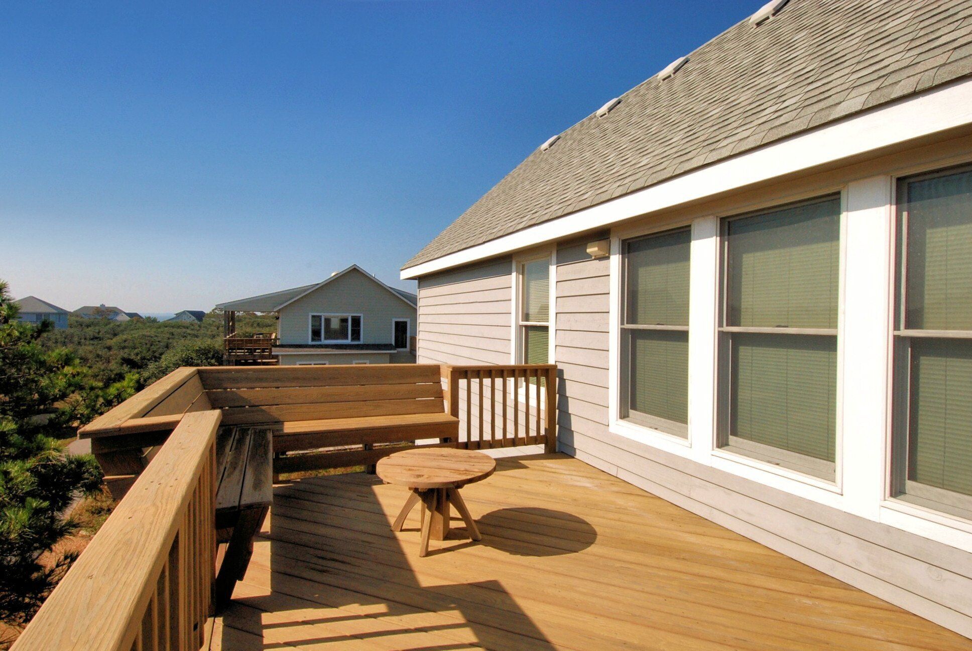 A wooden deck with a table and chairs, overlooking a residential area with houses and a clear sky.