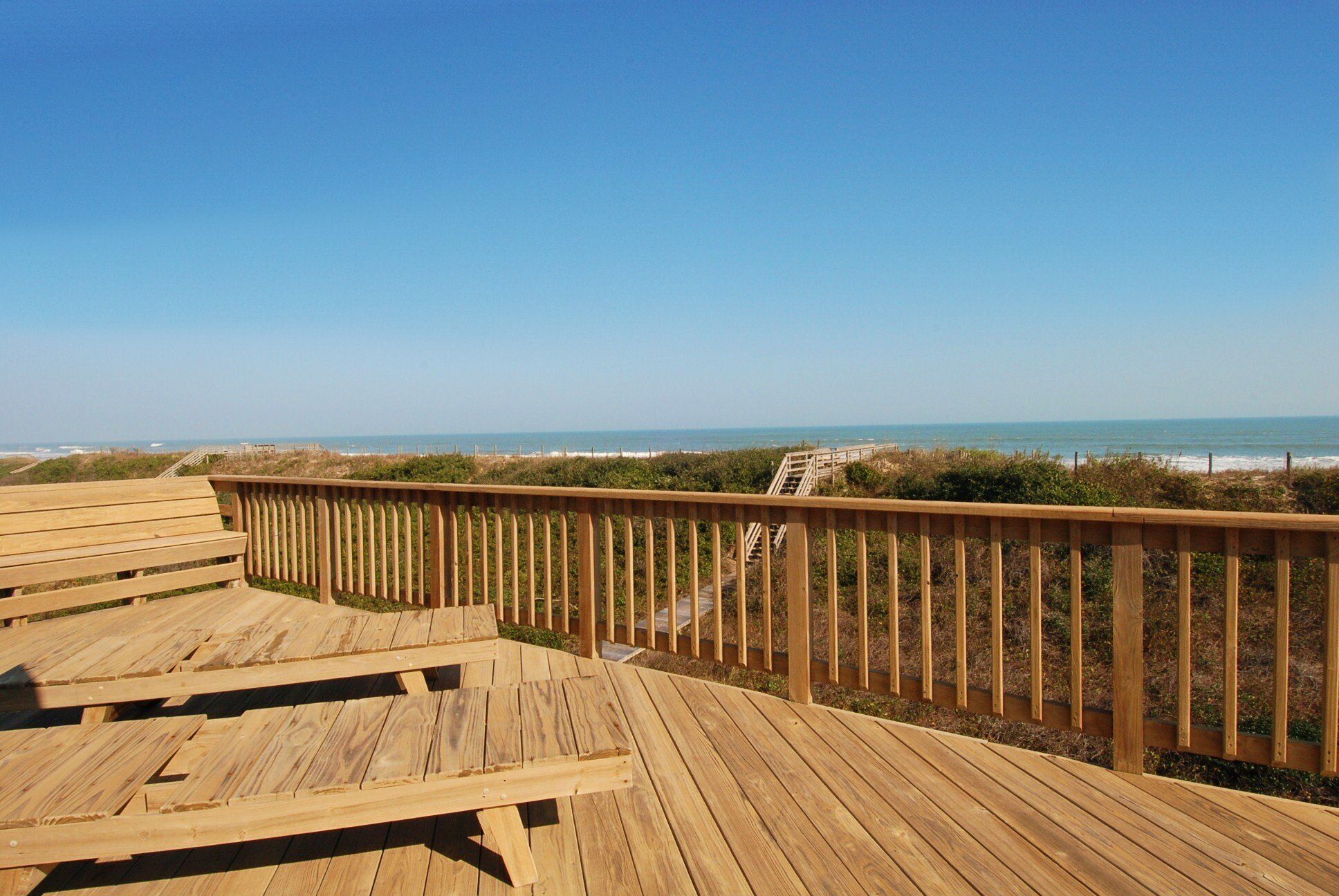 A wooden deck with benches overlooking a beach.