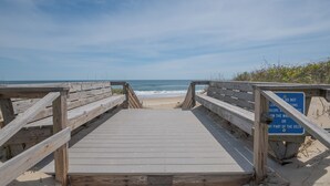 Pasarela de madera que lleva a una playa con cielo despejado.
