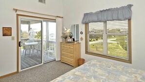 Un dormitorio con una puerta corrediza de vidrio a un balcón, un aparador, una cama y una ventana con vistas a un paisaje verde.