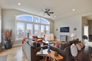 A spacious living room with a large window, a ceiling fan, and a cozy seating area with a sofa and chairs.