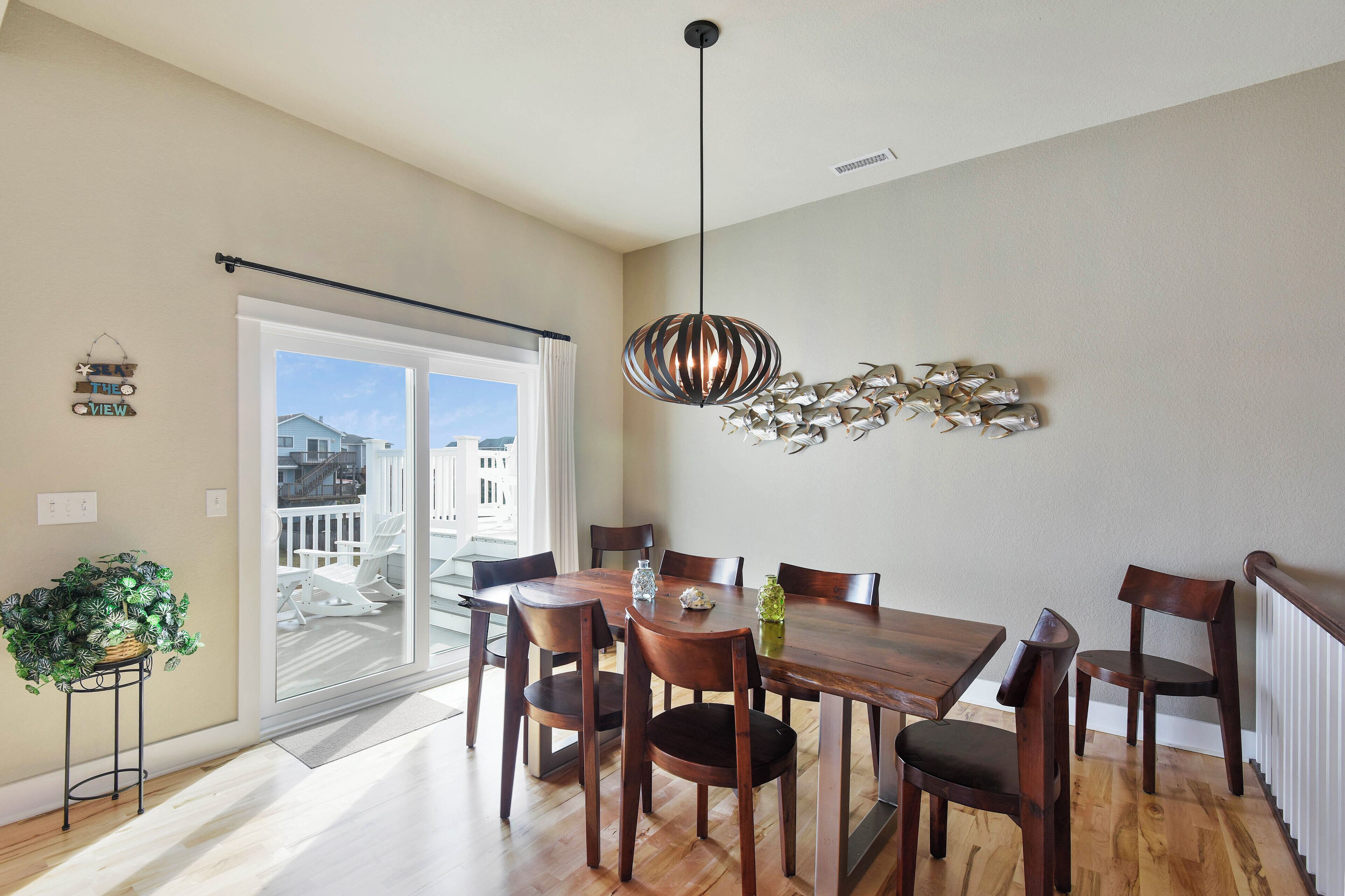 Un coin repas avec une table et des chaises en bois, un luminaire suspendu et une vue sur le balcon extérieur.