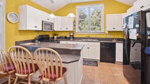 A kitchen with white cabinets, a granite countertop, a microwave, a stove, a sink, and a refrigerator. There are two wooden chairs with red cushions. - 4620- Flip Flop Inn, Private Pool + Hot Tub Near the Beach (Southern Shores)