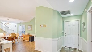 A dining area with a wooden table and chairs, a kitchen area with a refrigerator, and a hallway with a white door and a doormat. - 4620- Flip Flop Inn, Private Pool + Hot Tub Near the Beach (Southern Shores)
