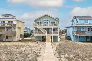 Situated on a sandy beach, this beachfront property features a two-story building with a staircase and a balcony on the upper level.