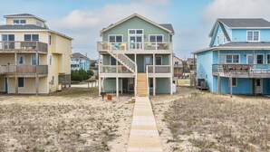 Une propriété située en bord de mer, avec un bâtiment principal doté d’un escalier menant à un balcon du deuxième étage, flanqué de deux autres bâtiments.