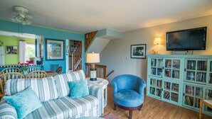 Ein Wohnzimmer mit einem gestreiften Sofa, einem blauen Sessel, einem Bücherregal und einem Fernseher.