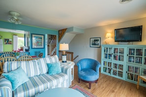 Ein Wohnzimmer mit einem gestreiften Sofa, einem blauen Sessel, einem Bücherregal und einem Fernseher.