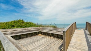 Ein hölzerner Steg führt zu einem Strand bei blauem Himmel.