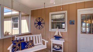 En mysig veranda med en vit gungstol, ett litet bord med en modell av en segelbåt och en kompass som väggdekoration.