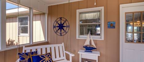 A cozy porch with a white swing, a small table with a sailboat model, and a compass wall decoration.