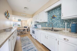 A modern kitchen with white cabinets, a blue mosaic backsplash, a stainless steel sink, and a coffee maker. - 4218- The Scotts' SandBar,  community pool and tennis, direct beach access, and more! (Duck)
