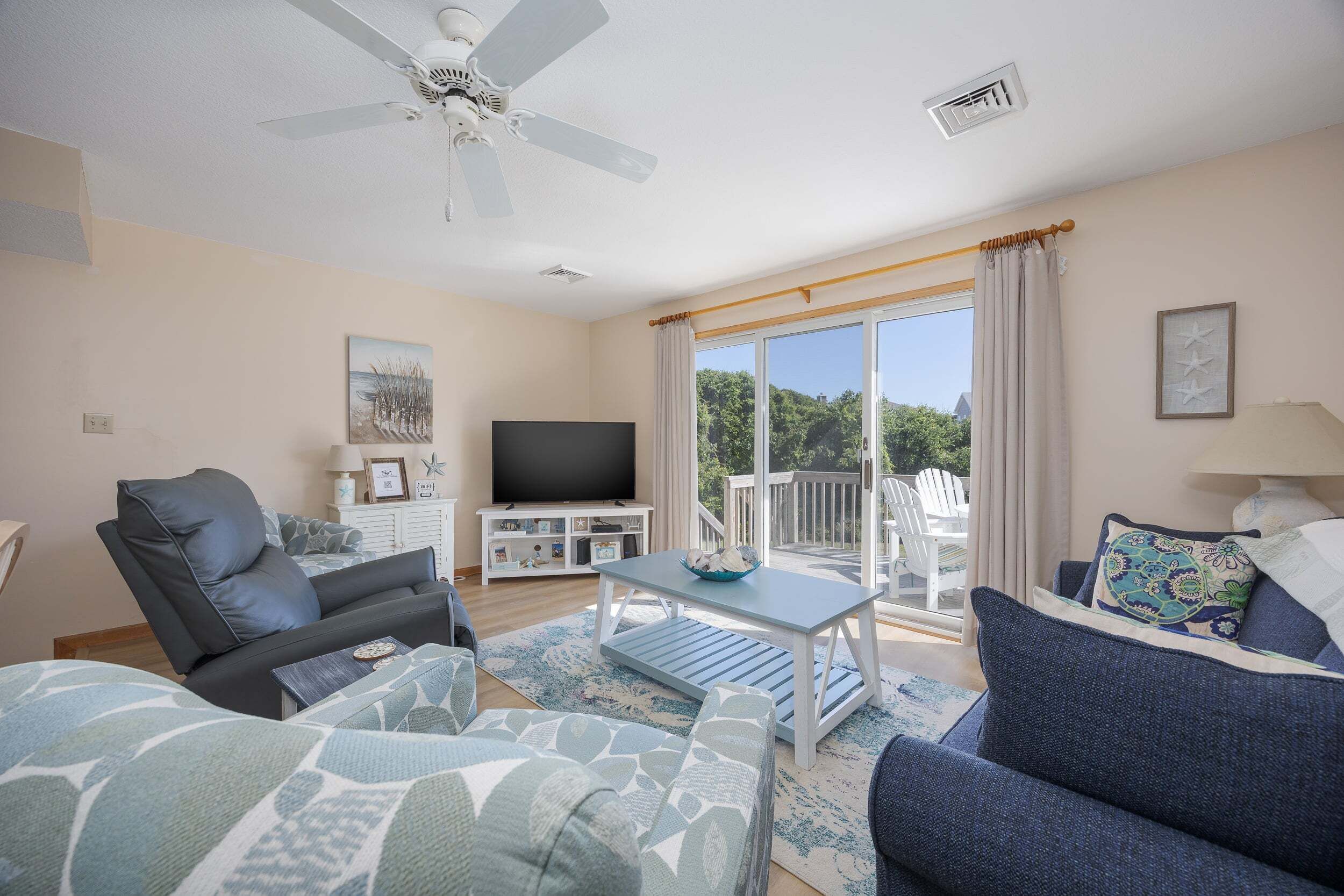 Ein Wohnzimmer mit Sofa, Sessel, Fernseher, Tisch und einem Balkon mit Gartenmöbeln.