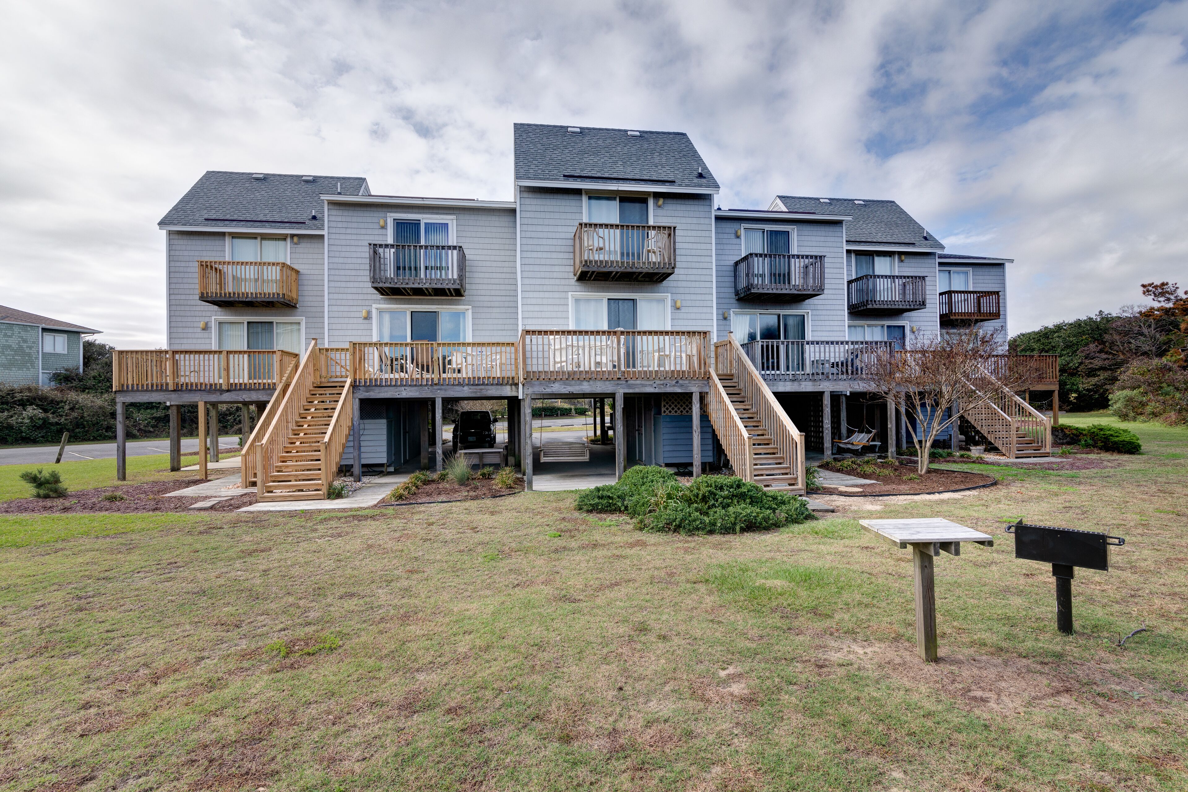 A multi-story residential building with balconies, a covered outdoor area, and a grassy yard.