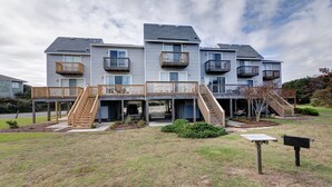 A multi-story residential building with balconies, a covered outdoor area, and a grassy yard. - 4218- The Scotts' SandBar - Oceanside Duck Condo Near Beach & Dining (Duck)