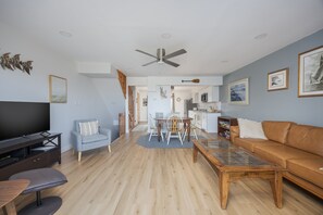 A modern living room with a flat-screen TV, a sofa, a coffee table, and a dining area with chairs and a table.