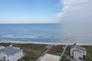 A coastal residential area with a view of the ocean, a sandy beach, and two houses with a pathway leading to the beach.
