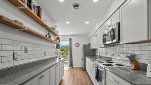 Una cocina moderna con armarios blancos, una estufa de acero inoxidable y un microondas. Hay estantes de madera sobre la encimera con libros y adornos.