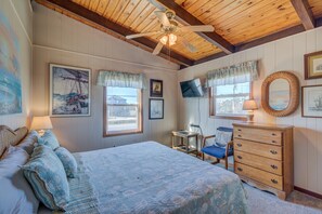A bedroom with a large bed, a wooden dresser, a desk, and a ceiling fan.