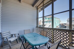 A covered outdoor area with a wooden table and chairs, a view of buildings through large windows.