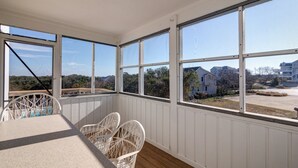 Une pièce baignée de lumière, avec de grandes fenêtres, des chaises en osier blanches et une terrasse en bois.