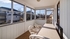 Un balcon abrité, doté de chaises en osier blanc, de grandes fenêtres et offrant une vue sur les maisons voisines.